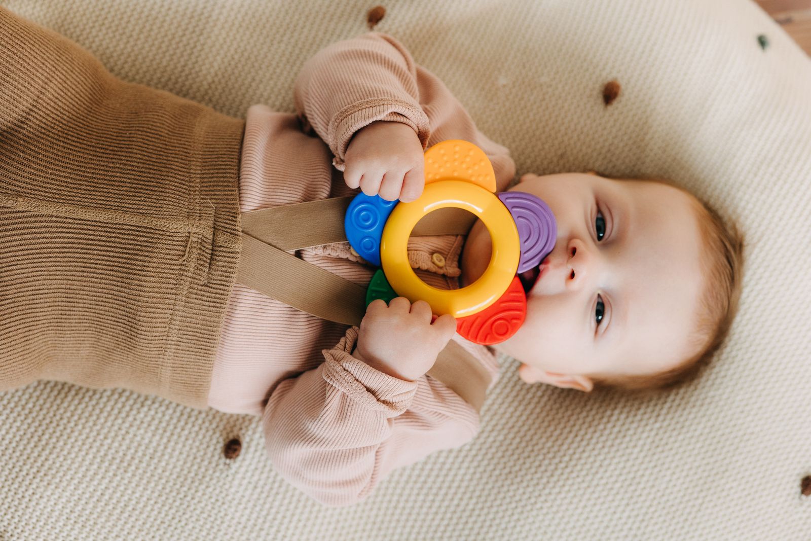 Un bébé mordille un anneau de dentition coloré, posé sur une surface douce