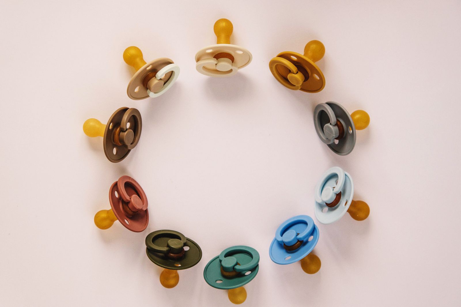 Sucettes (tétines) de bébé multicolores disposées en cercle sur une surface claire
