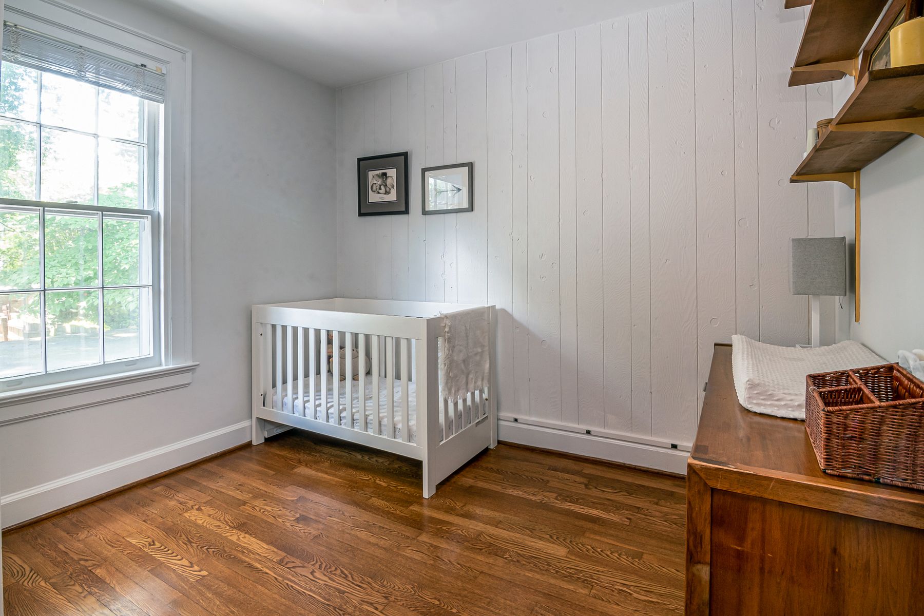 Lit à barreaux blanc avec son matelas dans une chambre de bébé lumineuse au parquet en bois